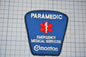 A blue emergency medical services patch with the word "PARAMEDIC" and the word "EMERGENCY MEDICAL SERVICES" printed on it, along with a red cross symbol.