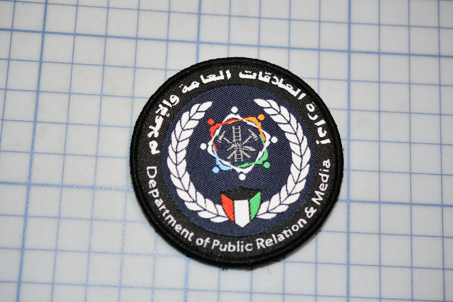 a circular patch with a logo and text, placed on a grid background.
