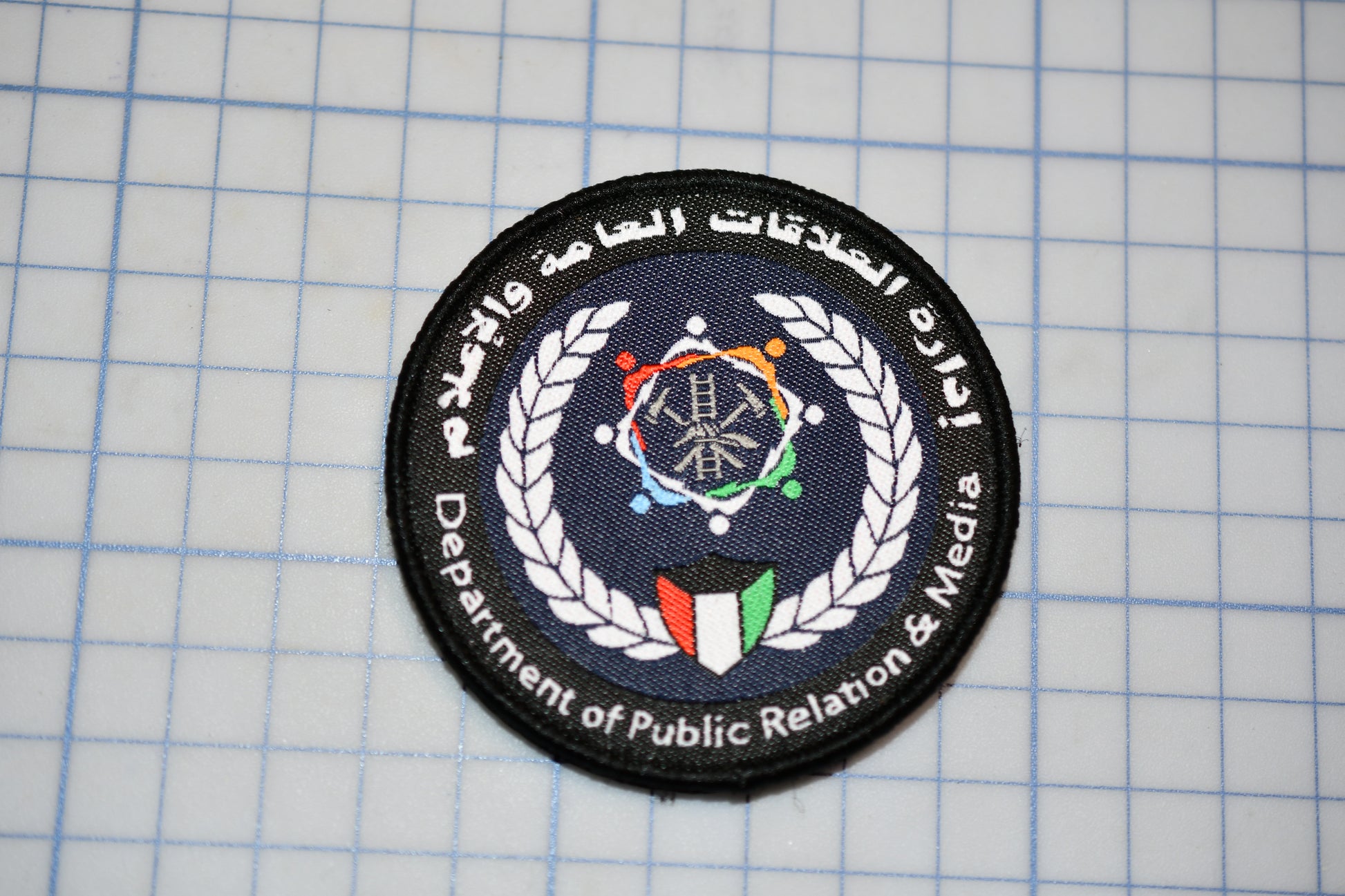 a circular patch with a logo and text, placed on a grid background.