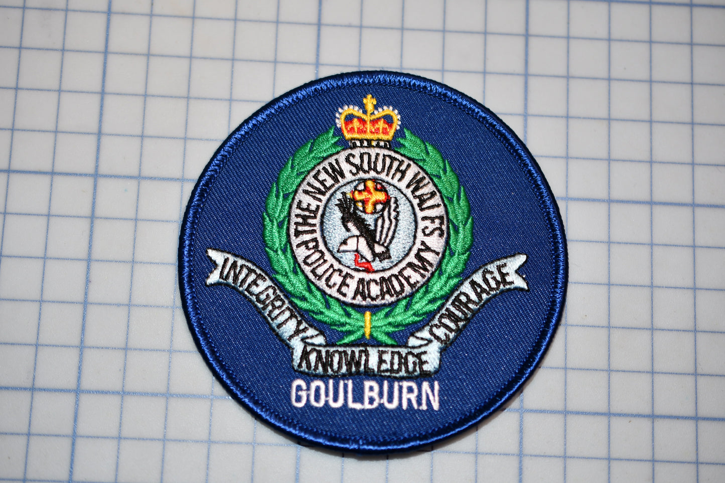 a blue circular patch with a crest and text, placed on a grid background.