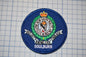 a blue circular patch with a crest and text, placed on a grid background.