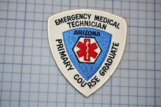 a patch with the text "EMERGENCY MEDICAL TECHNICIAN ARIZONA PRIMARY GRADUATE" and a red cross symbol, indicating that it is a patch for an emergency medical technician.