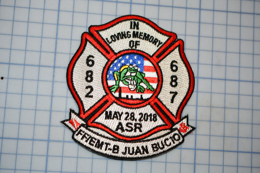 A patch with a red and white design, featuring a shield-like shape with a red border and a white border, and a graphic of a frog inside. The patch is embroidered with the text "IN LOVING MEMORY OF 682" and "MAY 28, 2018 ASR FEMT-B JUAN BUCIO".