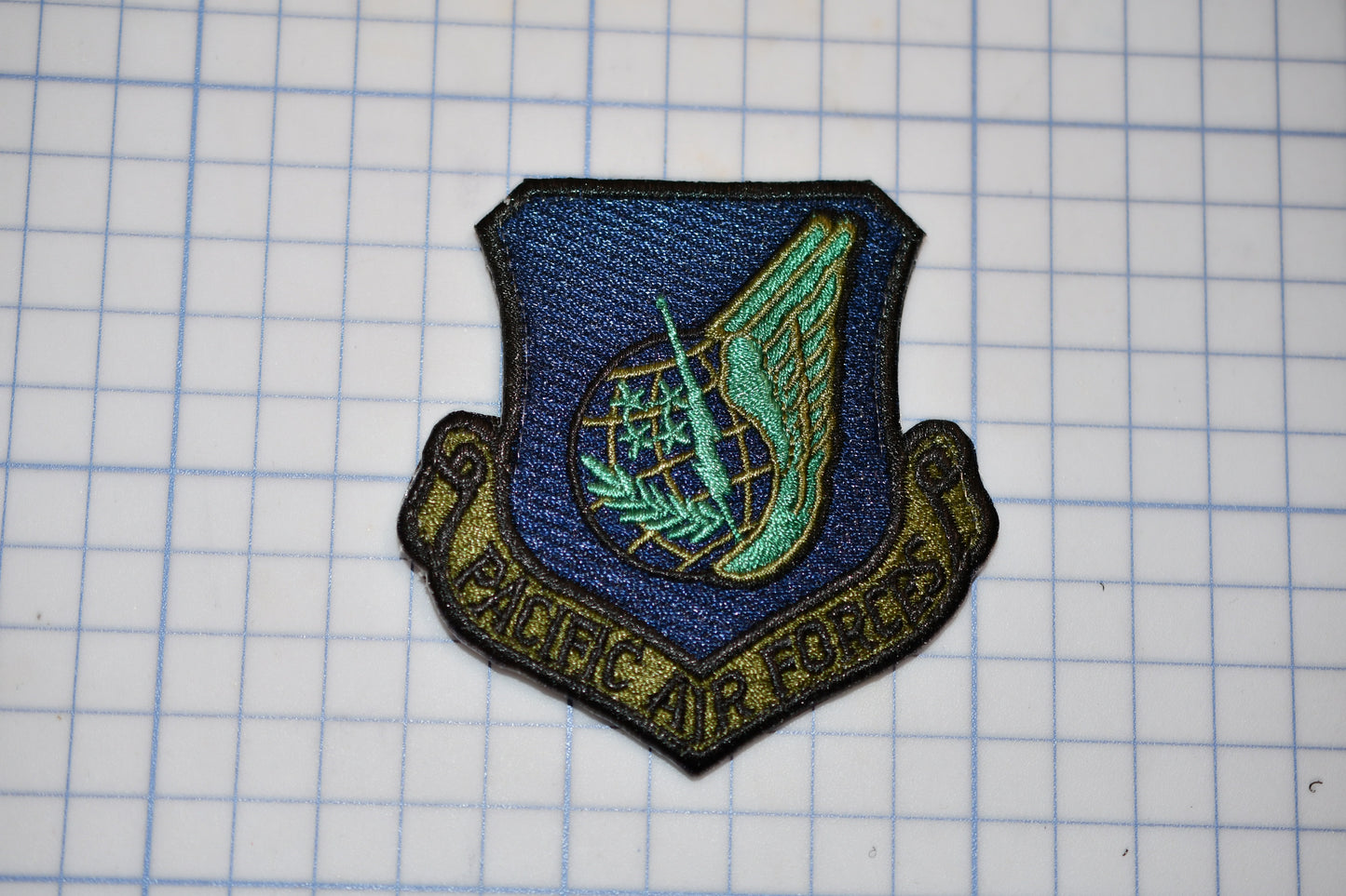 a military emblem with a winged symbol and the text "Pacific Air Force" on a grid background.