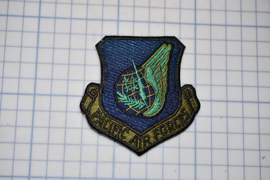 a military emblem with a winged symbol and the text "Pacific Air Force" on a grid background.