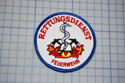 a circular patch with a red and blue design, including a snake, crossed swords, and a flame, surrounded by a blue border.