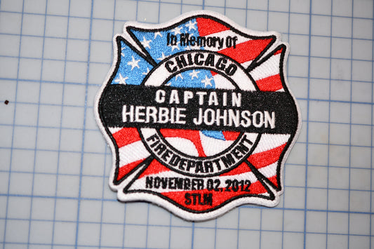 A patch with a design that includes a cross, an American flag, and text that says "In memory of CHICAGO CAPTAIN HERBIE JOHNSON FIRE DEPARTMENT NOVEMBER 02, 2012 STILM".