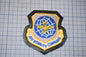 a military patch with a shield-shaped design, featuring a blue and yellow emblem with wings and a globe. The text "AIR MOBILITY COMMAND" is written below the emblem.