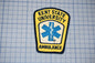 a yellow and blue patch with the text "KENT STATE UNIVERSITY AMBULANCE" and a medical symbol, indicating that it is a patch representing the Kent State University Ambulance Service.