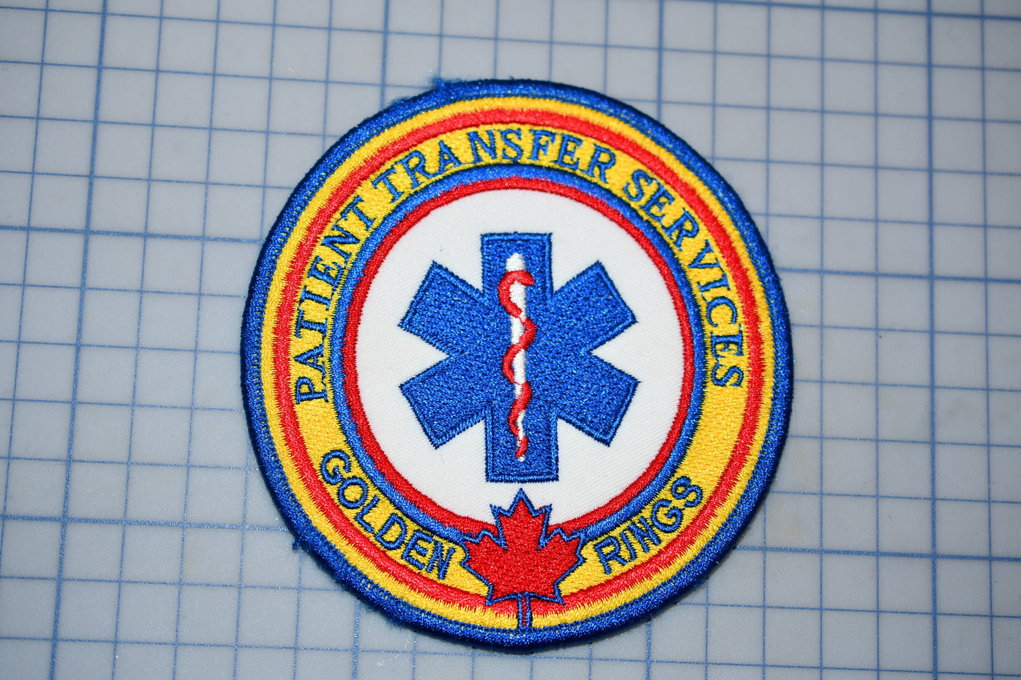 a circular patch with a blue and yellow border, displaying a medical symbol and text around it.