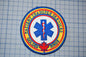 a circular patch with a blue and yellow border, displaying a medical symbol and text around it.