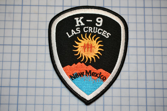 A black and white patch with the text "K-9 LAS CRUÑES" and an image of a sun with mountains in the background.