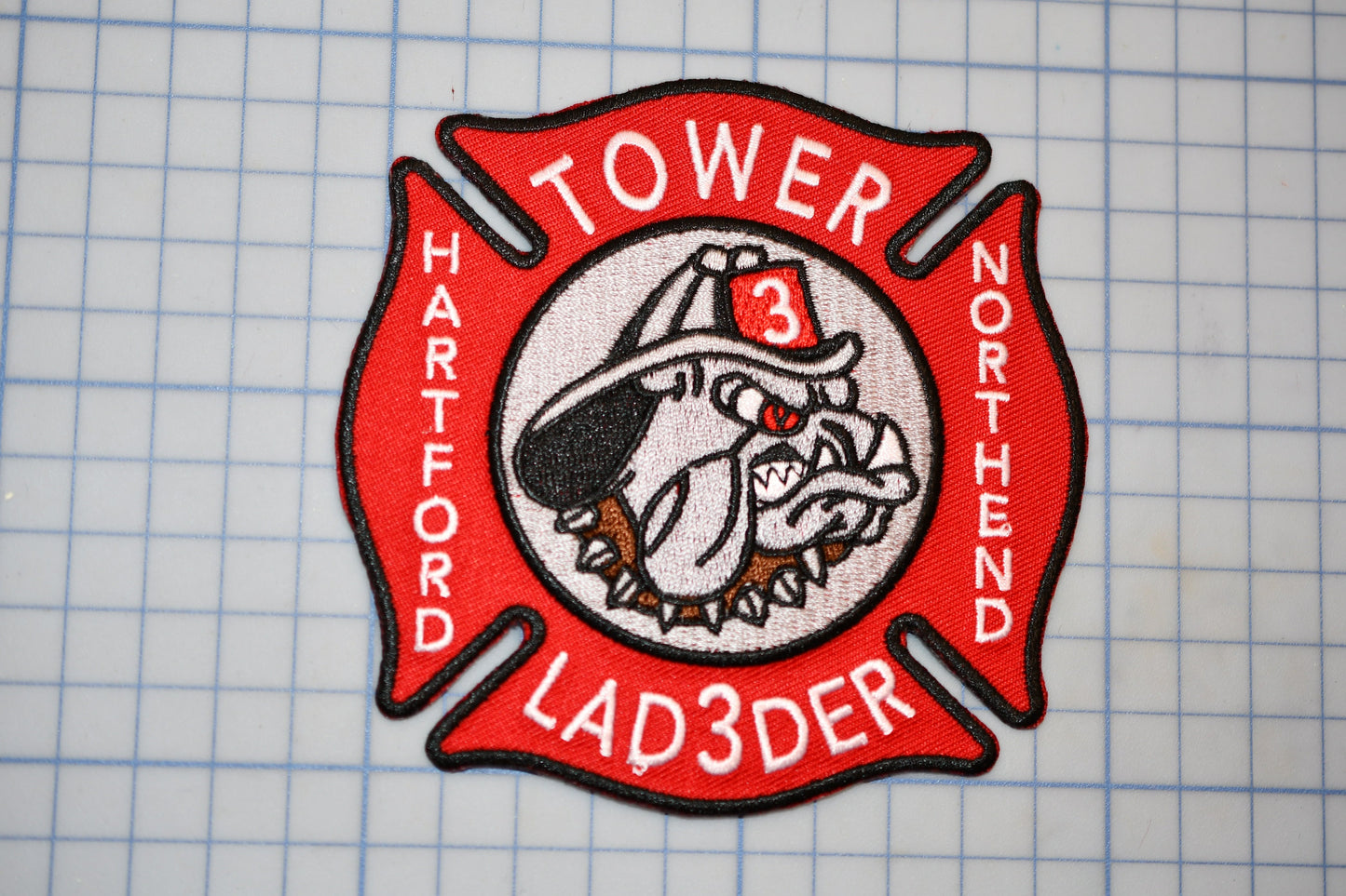 A red and white fire department patch with a bulldog emblem, representing the "Tower 3 Ladder" unit of the North Harvard Fire Department.