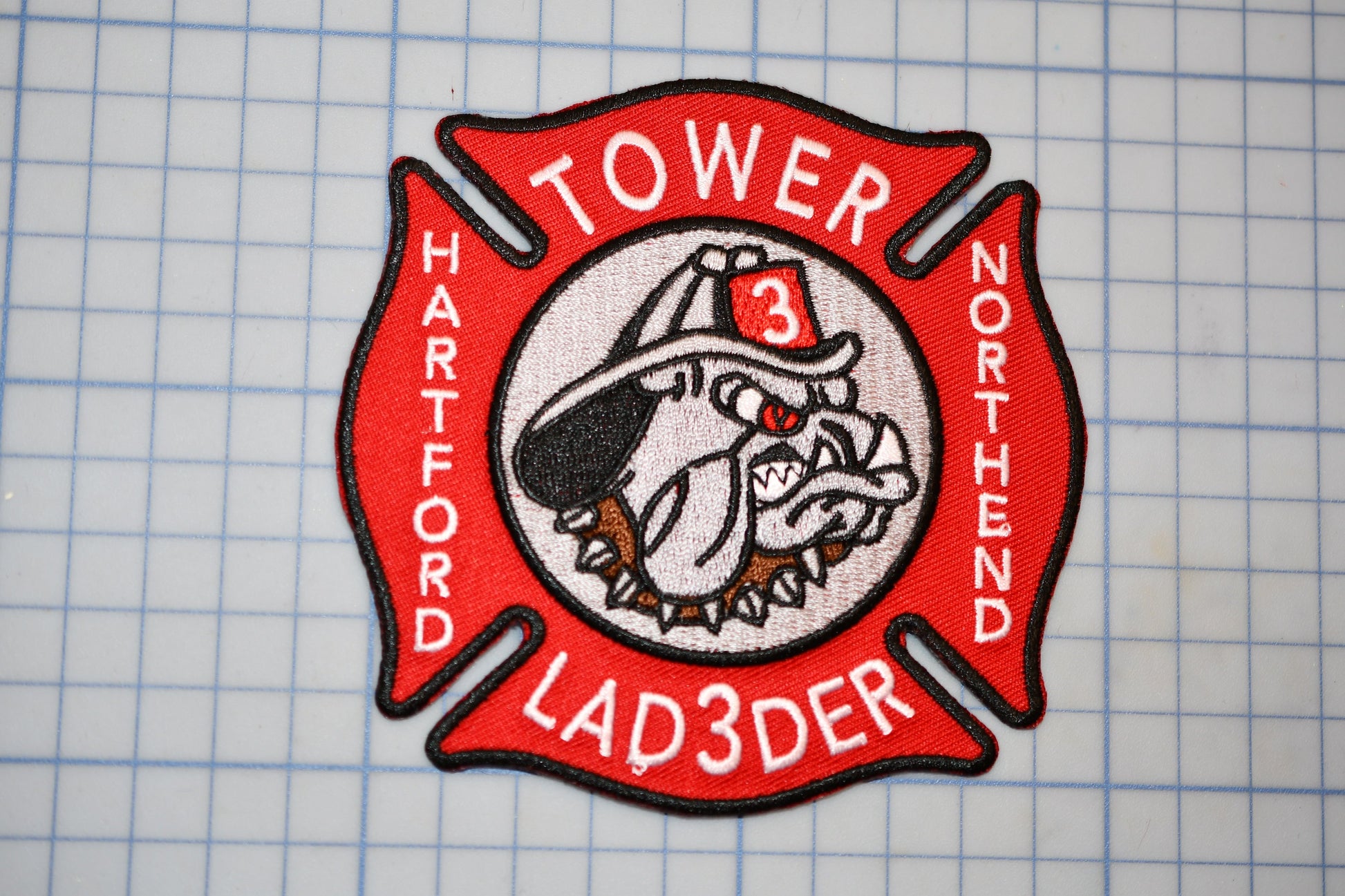 A red and white fire department patch with a bulldog emblem, representing the "Tower 3 Ladder" unit of the North Harvard Fire Department.