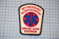 a patch with the text "Rettungsdienst Krankenttransport" and "Ambulanz-Aicher Rosenheim" printed on it, along with a medical symbol.