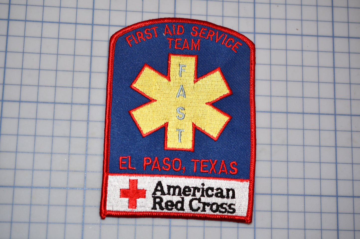 a patch with the text "Fast Aid Service Team" and "El Paso, Texas" written on it, along with a red cross symbol. The patch also displays the text "American Red Cross" at the bottom.