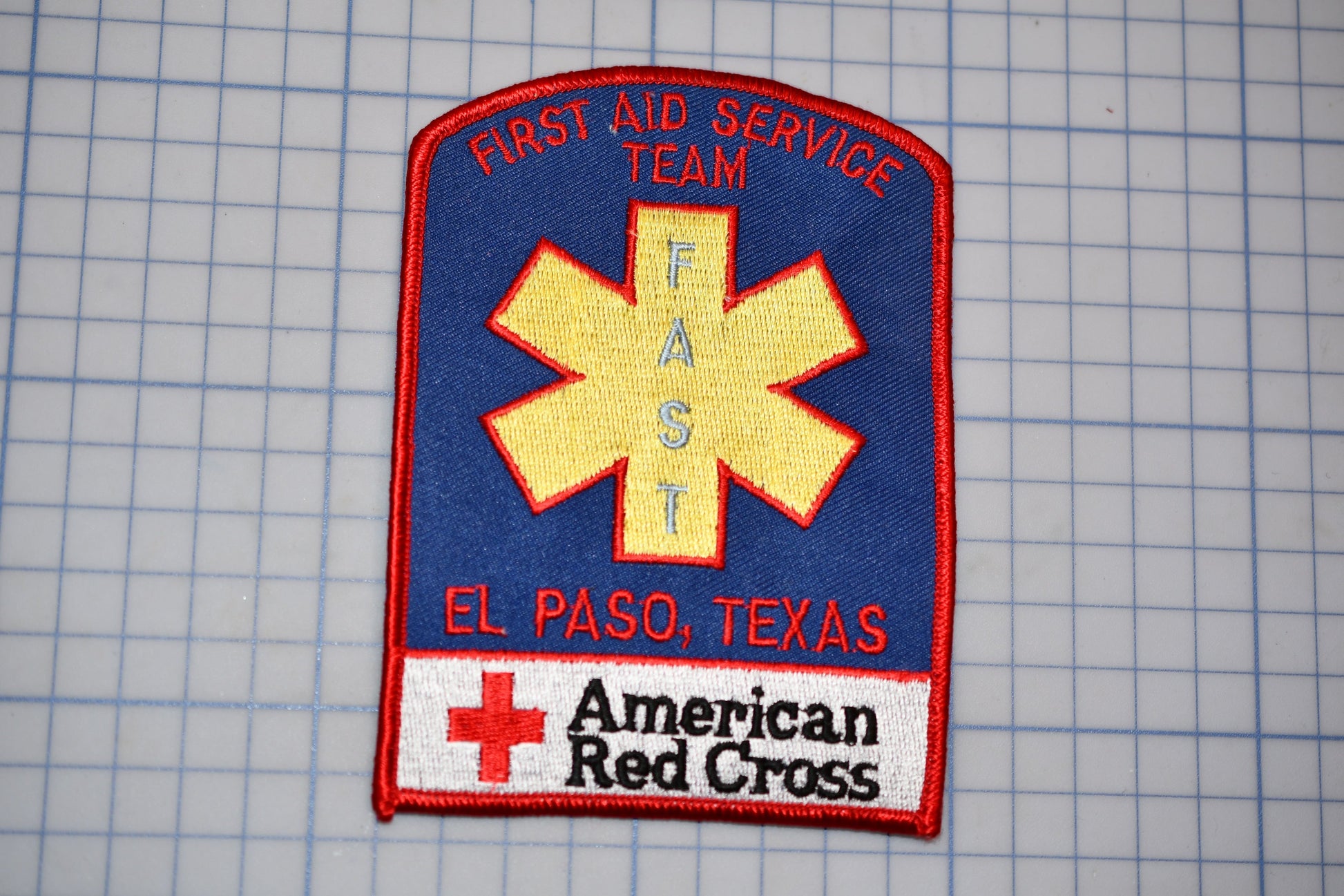 a patch with the text "Fast Aid Service Team" and "El Paso, Texas" written on it, along with a red cross symbol. The patch also displays the text "American Red Cross" at the bottom.