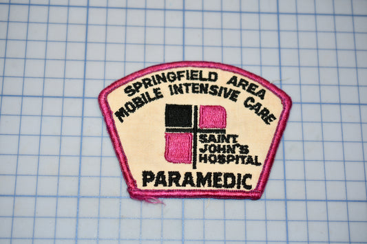 a patch with the text "Springfield Mobile Intensive Care Saint John's Hospital Paramedic" printed on it, along with a logo consisting of a pink cross on a beige background.