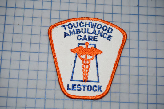 a patch with the text "TOUCHWOOD AMBULANCE CARE LESSTOCK" and an orange medical symbol, likely representing Touchwood Ambulance Care.