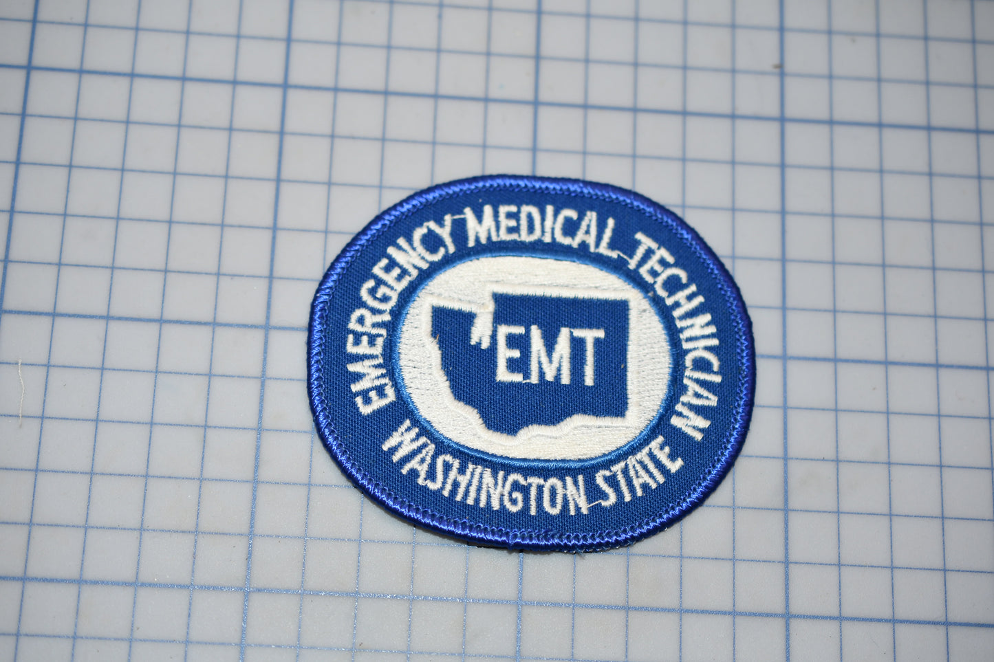 A blue and white patch with the text "EMT Washington State" on it, indicating that it is an Emergency Medical Technician (EMT) patch from the state of Washington.