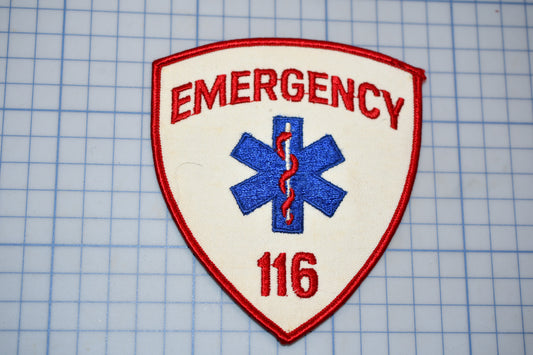 a red and white emergency medical patch with the number "116" on it, placed on a blue grid background.