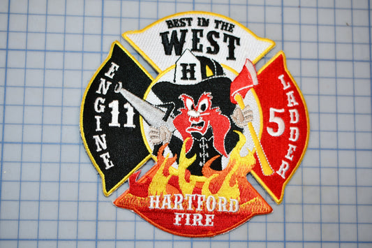 A fire department patch with a cartoon firefighter character, surrounded by flames and text indicating the department's name and location.
